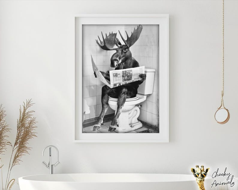 May include: A black and white photo of a moose sitting on a toilet and reading a newspaper. The moose is wearing a serious expression and has large antlers. The photo is framed in a white frame.
