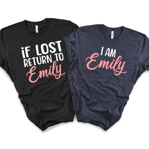 May include: Two t-shirts, one black and one navy blue, with a matching design. The black t-shirt says "if lost return to Emily" in white text with "Emily" in pink. The navy blue t-shirt says "I am Emily" in white text with "Emily" in pink.