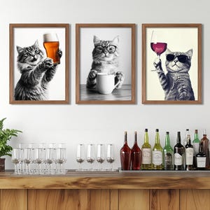 Peut inclure: Trois impressions encadrées de chats savourant des boissons. La première impression montre un chat tenant un verre de bière. La deuxième impression montre un chat tenant une tasse de café. La troisième impression montre un chat tenant un verre de vin.
