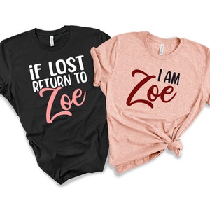 May include: Two t-shirts, one black and one peach, with the text "if lost return to Zoe" in white and pink on the black shirt and "I am Zoe" in burgundy on the peach shirt.