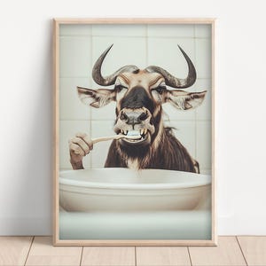 May include: Framed print showing a wildebeest brushing its teeth in a bathroom. The animal has large, curved horns and is holding a toothbrush. The background features a tiled wall and a white sink.