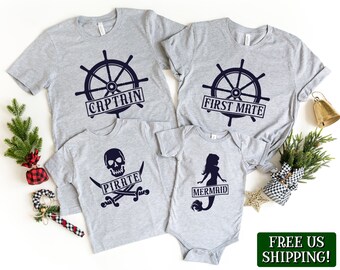 May include: A set of four grey t-shirts with nautical themed designs. The shirts feature a steering wheel with the words "Captain", "First Mate", "Pirate", and "Mermaid".