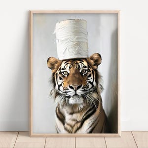 Op de afbeelding: Een ingelijste print met een tijger met een toiletpapierrol als hoed. De tijger heeft een bruin en zwart gestreepte vacht, met een geconcentreerde blik. De achtergrond is lichtgrijs en de lijst is licht van hout.