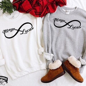 May include: Two grey sweatshirts with an infinity symbol design. The symbol has the names "Maya" and "Lucas" written on each side.