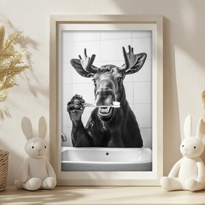 May include: A black and white photo of a moose with its mouth open, holding a toothbrush in its mouth. The moose is in a bathroom setting with a white sink and tiled walls.