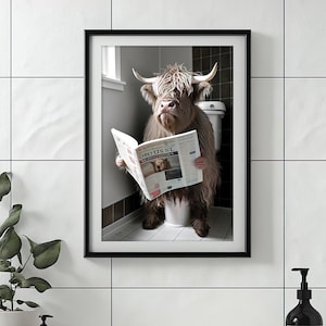 May include: Framed art print featuring a Highland cow sitting on a toilet, reading a newspaper. The cow has long, shaggy brown fur and large horns. The newspaper has the text "ORO USST". The artwork is framed in a black frame.