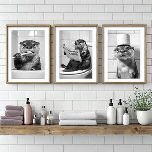 May include: Three black and white framed prints of otters. The otter in the left print is holding a toothbrush. The otter in the center print is reading a newspaper. The otter in the right print is wearing a toilet paper roll as a hat.