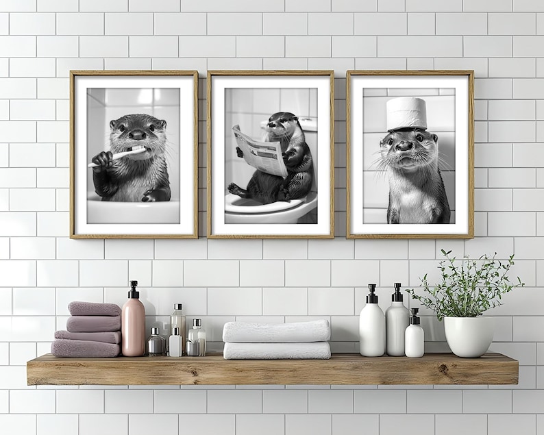 May include: Three black and white framed prints of otters. The otter in the left print is holding a toothbrush. The otter in the center print is reading a newspaper. The otter in the right print is wearing a toilet paper roll as a hat.