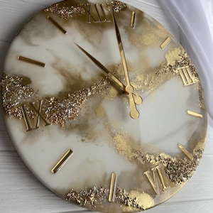 May include: A white and gold resin clock with Roman numeral markings and gold glitter accents. The clock hands are gold.