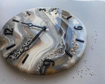 May include: A round clock with black hands and black numbers on a white, gray, and brown background with gold glitter. The clock face has a marbled, abstract design.