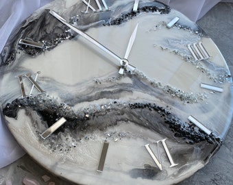 May include: A white and gray resin clock with Roman numeral markings and silver hands. The clock face has a marbled design with silver glitter embedded in the resin.