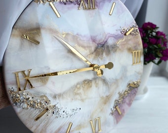 May include: White and gold resin clock with Roman numeral markings and a marble-like design. The clock face is decorated with small, clear crystals.
