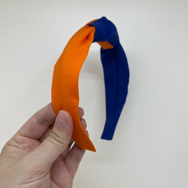May include: A blue and orange knotted headband. The headband is made of fabric and has a simple design.