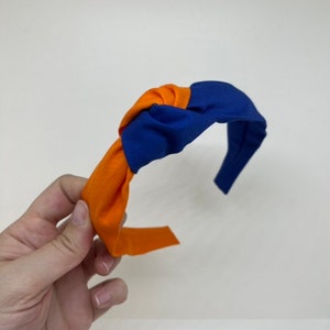 May include: A blue and orange knotted headband. The headband is made of fabric and has a simple design.