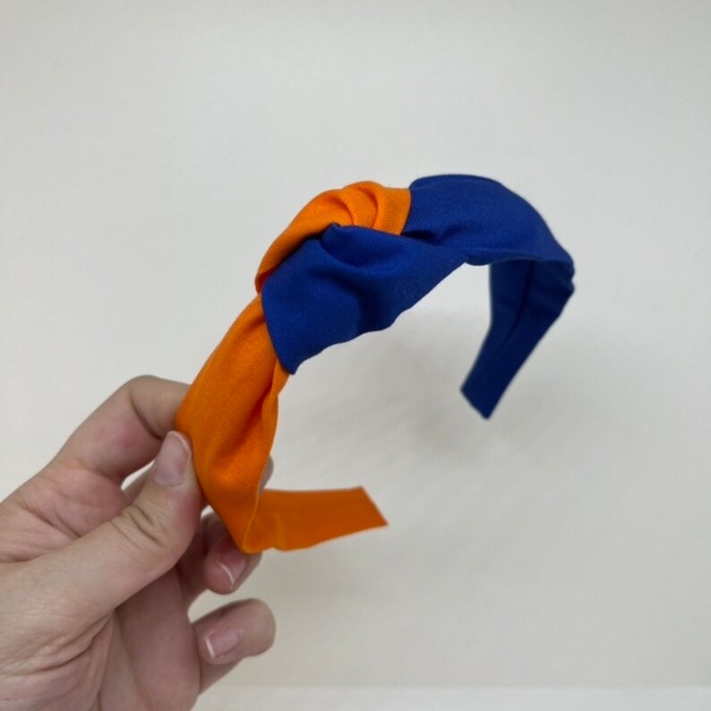 May include: A blue and orange knotted headband. The headband is made of fabric and has a simple design.