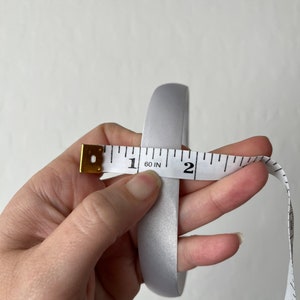 May include: A silver satin ribbon measured with a tape measure, showing a length of 1 and 60/100 inches.