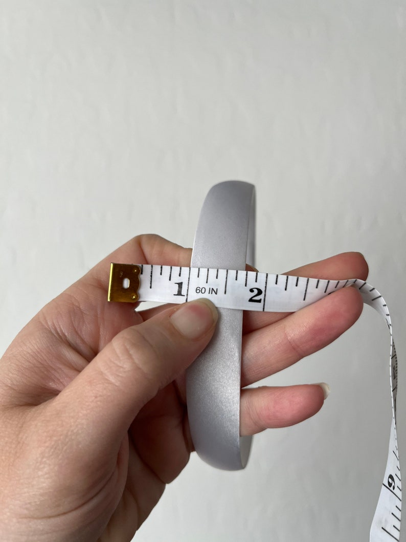 May include: A silver satin ribbon measured with a tape measure, showing a length of 1 and 60/100 inches.