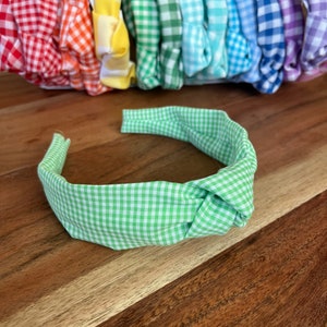 Könnte beinhalten: Ein grünes und weißes kariertes Knotenhaarband. Das Haarband ist aus Stoff und hat ein schlichtes Design.
