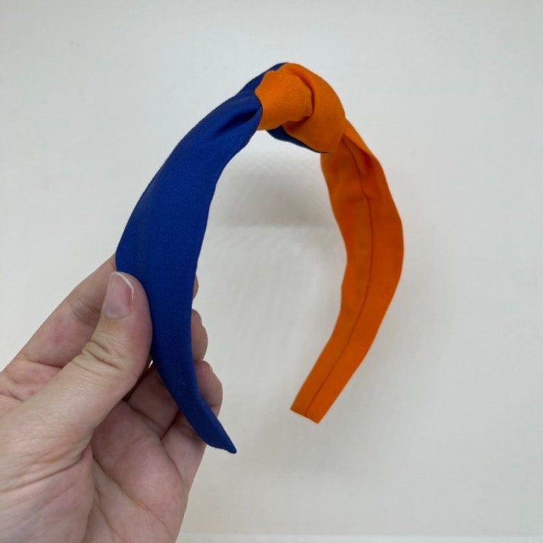 May include: A blue and orange knotted headband. The headband is made of fabric and has a simple design.