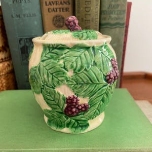 Peut inclure: Pot en céramique avec couvercle, base crème et feuilles vertes avec des baies violettes. Le pot a une poignée en forme de baie sur le couvercle. Le design est de style classique et vintage.