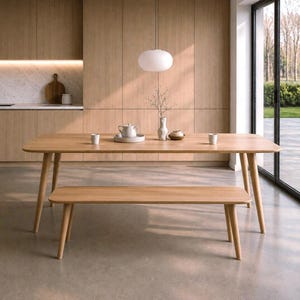 Può includere: Un tavolo da pranzo in legno chiaro con angoli arrotondati e quattro gambe affusolate, accompagnato da una panca in legno abbinata con quattro gambe affusolate. Il piano del tavolo ospita due piccole tazze bianche, una teiera bianca su un vassoio e un vaso bianco.