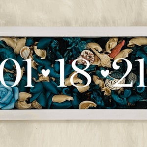 May include: White framed box with a blue and brown floral arrangement inside. The date "01 18 21" is displayed in white lettering.