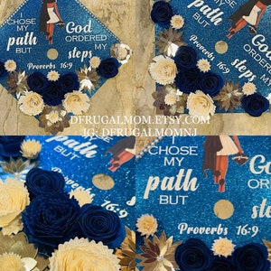 Op de afbeelding: Een blauwe afstudeerhoed versierd met gouden glitter, witte en blauwe papieren bloemen en een zwart silhouet van een vrouw. De hoed heeft de tekst "I chose my path but God ordered my steps Proverbs 16:9" erop.