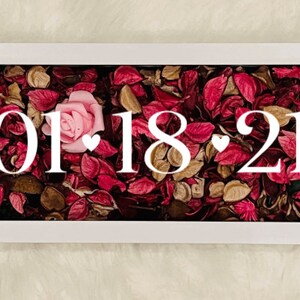 May include: A white frame with a glass front filled with dried rose petals and a single pink rose. The date "01.18.21" is displayed in white lettering.