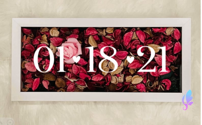 May include: A white frame with a glass front filled with dried rose petals and a single pink rose. The date "01.18.21" is displayed in white lettering.