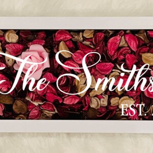 Puede incluir: Caja enmarcada en blanco con una rosa rosa y p&eacute;talos de flores secas. El texto "The Smiths EST. 2021" se muestra en la caja.