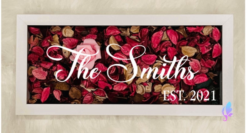 Puede incluir: Caja enmarcada en blanco con una rosa rosa y p&eacute;talos de flores secas. El texto "The Smiths EST. 2021" se muestra en la caja.