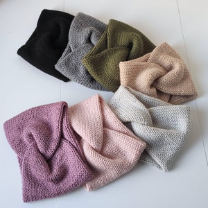 May include: A set of eight knitted headbands in various colours, including black, grey, green, beige, pink, and purple. Each headband has a knotted design.