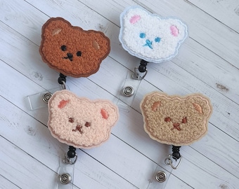 May include: Four fuzzy teddy bear-shaped badge holders with retractable reels. The bears are brown, beige, pink, and white.