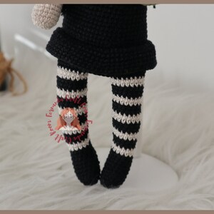 May include: Crocheted doll with black and white striped leggings. The doll is wearing a black dress and has a white crocheted head.