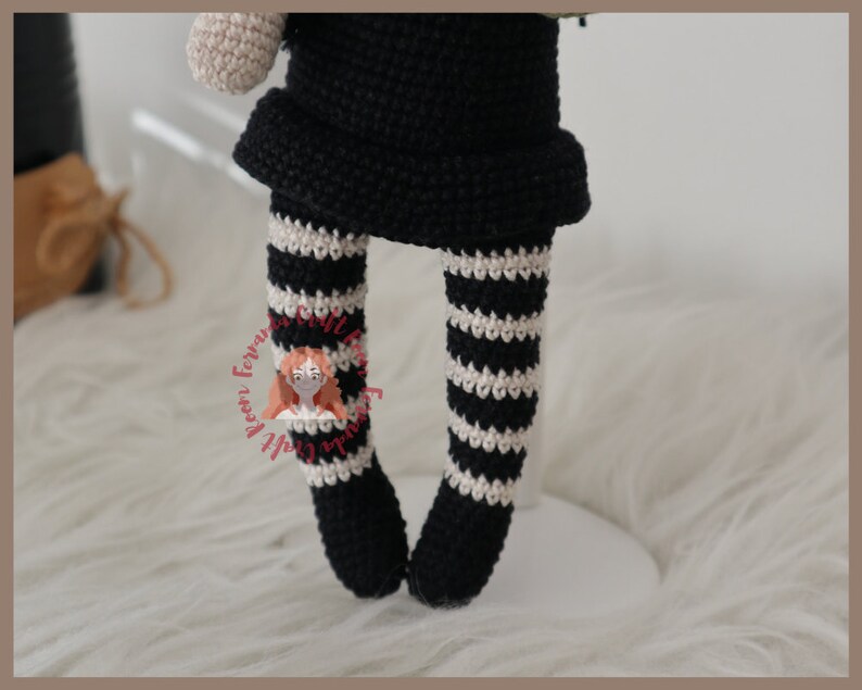 May include: Crocheted doll with black and white striped leggings. The doll is wearing a black dress and has a white crocheted head.