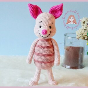 Può includere: Un giocattolo amigurumi a forma di maiale rosa lavorato a uncinetto con un corpo a righe rosa e bianco. Il giocattolo ha un naso rosa e un viso sorridente.
