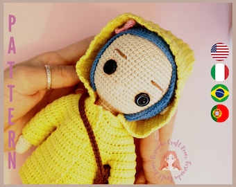 May include: Crocheted doll wearing a yellow raincoat with a brown strap and a blue hooded hat. The doll has black button eyes and a neutral expression.