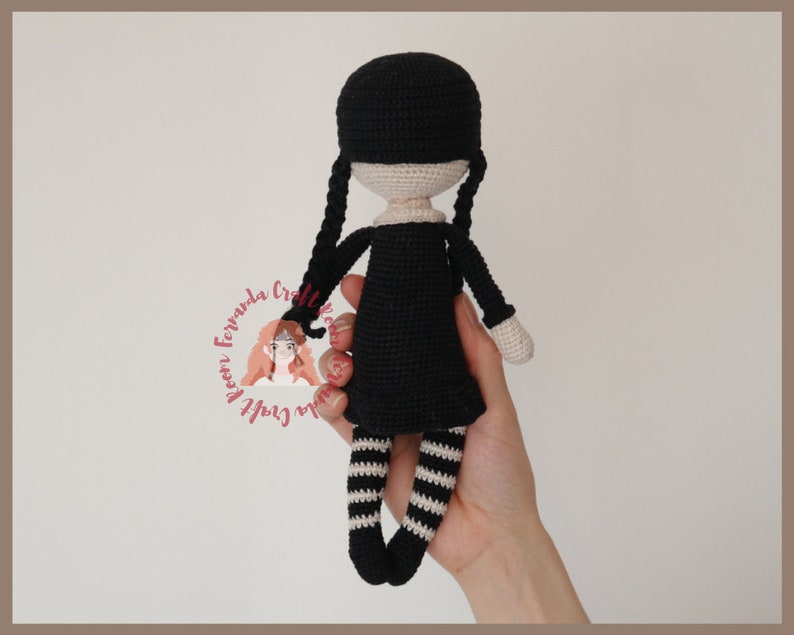 May include: Black crochet doll with white stripes on the legs and black pigtails. The doll is wearing a black dress.