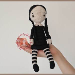 May include: Crocheted doll with black hair in pigtails, wearing a black dress with white stripes and black and white striped stockings.