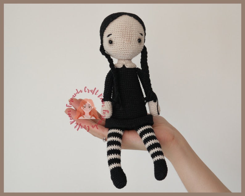 May include: Crocheted doll with black hair in pigtails, wearing a black dress with white stripes and black and white striped stockings.