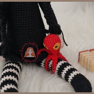 May include: A black and white striped crocheted doll with a red crocheted octopus sitting on its lap. The doll is wearing a black dress and has a white crocheted hat.
