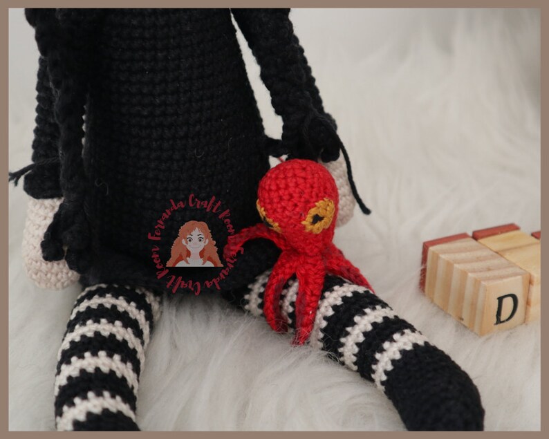 May include: A black and white striped crocheted doll with a red crocheted octopus sitting on its lap. The doll is wearing a black dress and has a white crocheted hat.