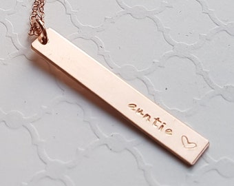 May include: A rose gold necklace with a bar pendant that says "auntie" with a small heart.