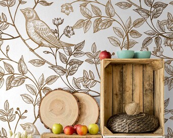 Op de afbeelding: Drie houten kratten op elkaar gestapeld tegen een witte muur met een gouden bloemen- en vogelbehang. De bovenste krat heeft twee blauwe kommen en een bol garen. De middelste krat heeft twee houten rondjes en appels. De onderste krat heeft een geweven mand en twee kleinere geweven manden.