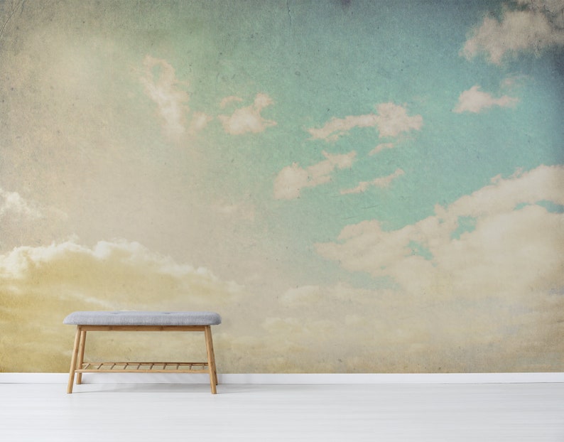 May include: A wall mural featuring a sky scene with fluffy white clouds against a backdrop of blue and yellow hues. A gray bench with wooden legs sits in front of the mural, adding a touch of functionality to the artistic display.