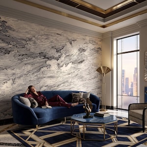 May include: A navy blue curved sofa with gold legs, a blue marble-topped hexagonal coffee table with a gold frame, and a patterned armchair. The room features a large wall mural with black and white swirling line art and a sunburst wall mirror.