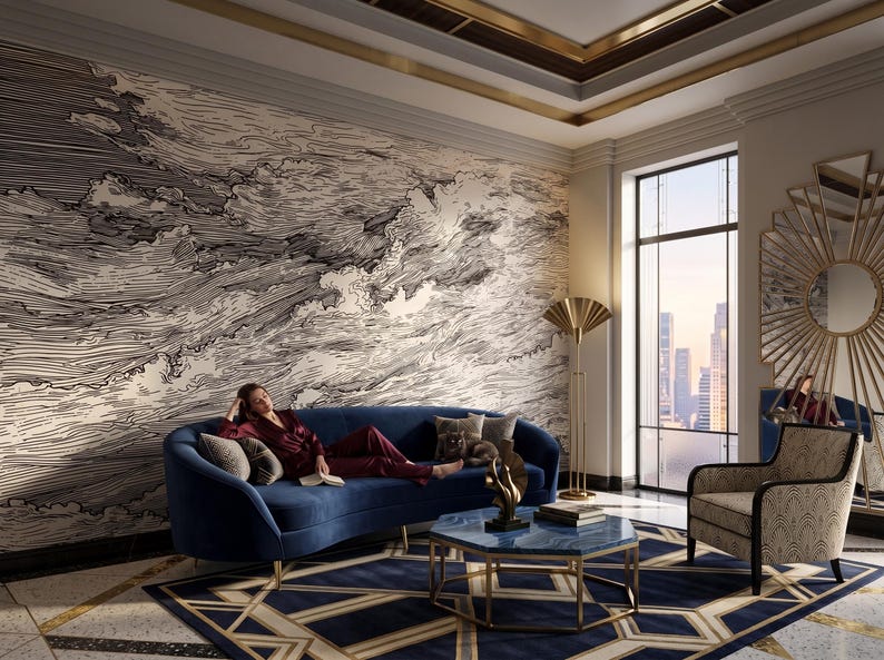 May include: A navy blue curved sofa with gold legs, a blue marble-topped hexagonal coffee table with a gold frame, and a patterned armchair. The room features a large wall mural with black and white swirling line art and a sunburst wall mirror.