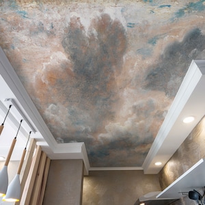 Può includere: Un soffitto bianco con un murale dipinto che rappresenta un cielo con nuvole in tonalità di blu, marrone e bianco. Tre lampadari pendenti bianchi con corde di legno pendono dal soffitto.