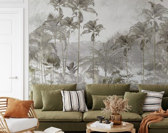 May include: A green sectional sofa with a variety of throw pillows, a coffee table with a book and a vase of dried flowers, and a woven chair with a throw pillow. The sofa is in front of a wall with a large mural of palm trees and a lake.