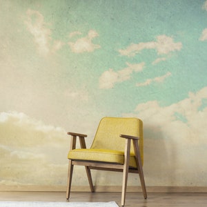May include: A yellow armchair with wooden arms and legs sits in front of a wall mural depicting a sky with clouds. A white rug is on the wooden floor in front of the chair. The chair has a mid-century modern design.